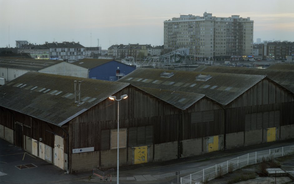 <p><strong>Gilles Saussier | <i>Itinéraire de </i>Patrice Corfmat, sur les traces de Didier Harel<br class='manualbr' />Saint-Nazaire | 2008</strong><br class='manualbr' /><i>Hangars, bassin de Saint-Nazaire </i>| Impression pigmentaire 85 x 128 cm<br class='manualbr' />éd. 1/3 + 2 EA | collection de l'artiste.</p>
<p><i>Enregistrés et photographiés, ces parcours se superposent et dessinent une autre topographie de Saint-Nazaire. Ils déplacent les questions de l'habiter (qui est dehors, qui est dedans ?) de l'étranger (comment devient-on étranger dans sa propre ville ?), de l'hospitalité (quels lieux d'accueil pour les SDF mais aussi pour l'art en prise avec les questions sociales ?)</i></p>